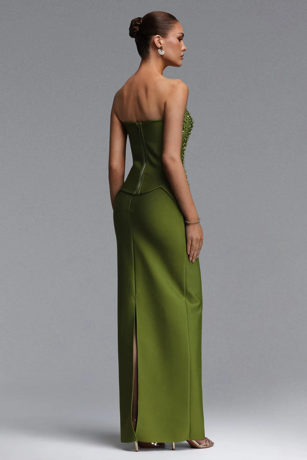 Woman wearing a strapless green evening gown with a slit on a gray background