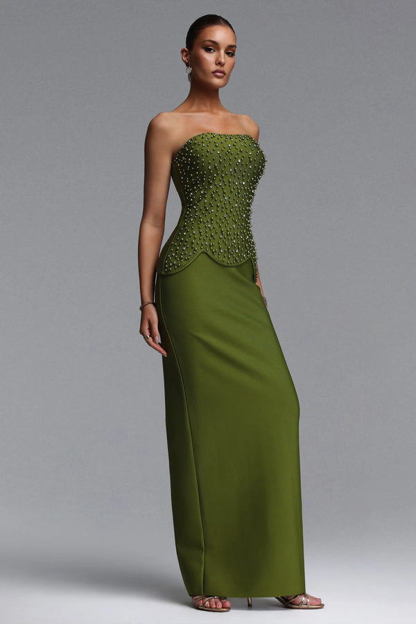 Woman wearing a strapless green evening gown with beaded top on a gray background