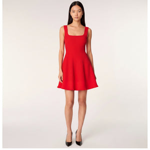 A model wearing a bright red sleeveless pleated dress with a square neckline and a flared skirt, set against a plain light gray studio background.