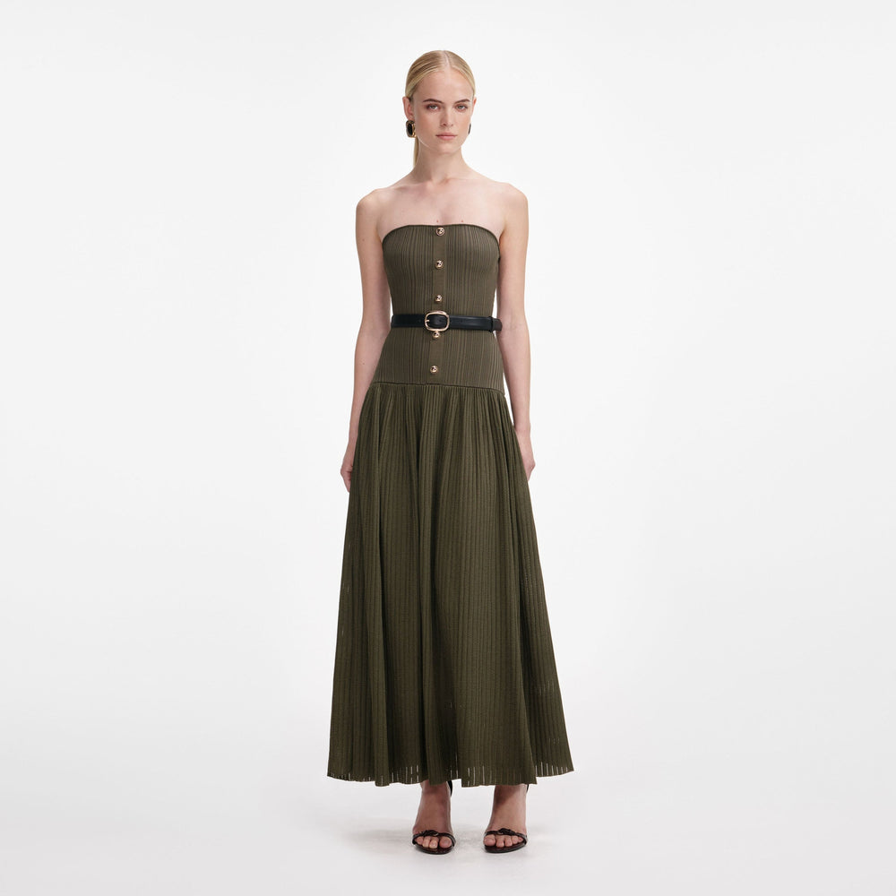 A woman modeling a strapless olive green pleated maxi dress with a black waist belt and gold-tone buckle, set against a plain white studio background.