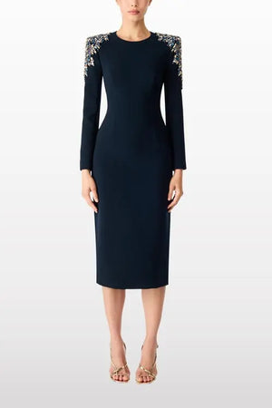 A model wearing a dark navy blue knee-length sheath dress with long sleeves and intricate silver beaded shoulder detailing, paired with nude high-heeled sandals against a light gray studio background.