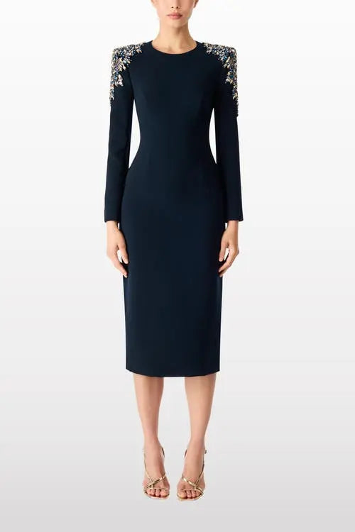 A model wearing a dark navy blue knee-length sheath dress with long sleeves and intricate silver beaded shoulder detailing, paired with nude high-heeled sandals against a light gray studio background.