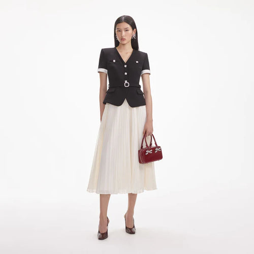 Woman wearing a black top and white skirt with a red handbag on a white background