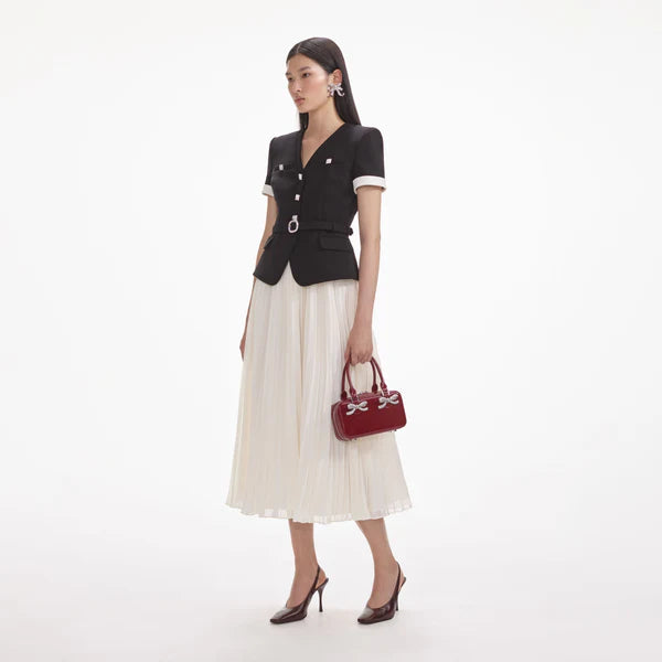 Woman wearing a black top and white skirt with a red handbag on a white background
