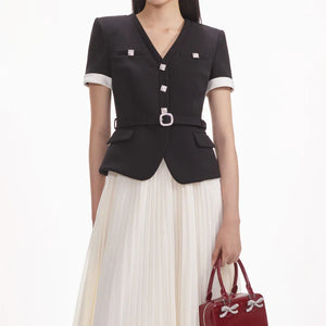 Woman wearing a black blazer with white trim and a red handbag on a white background