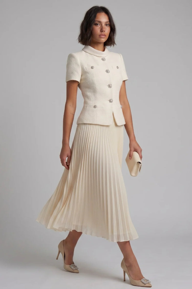 Woman wearing a cream-colored suit with a pleated skirt on a gray background