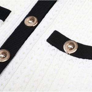 Close-up of a white textured fabric with black ribbons and gold buttons.