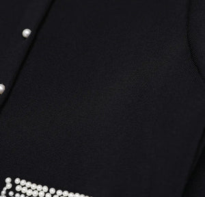 Close-up of a black garment with pearl buttons and trim