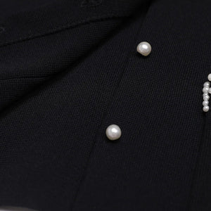 Close-up of a black garment with pearl buttons and embellishments.