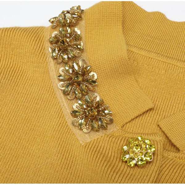 Mustard yellow sweater with floral embellishments on a white background