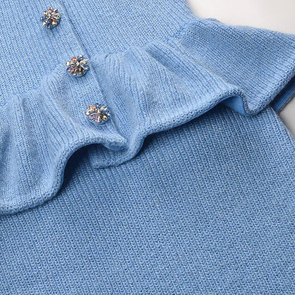 Blue knitted garment with ruffled collar and decorative buttons on a light background