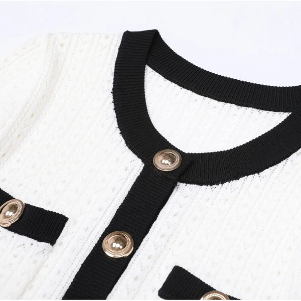 Close-up of a white garment with black collar and gold buttons on a light gray background