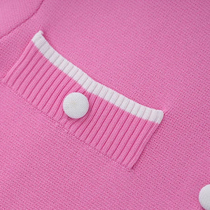 Close-up of a pink cardigan with a button on a pink background