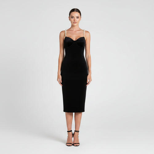 A woman modeling a black sleeveless bodycon midi dress with a sweetheart neckline and thin straps, paired with black strappy high-heeled sandals, against a light gray studio background.