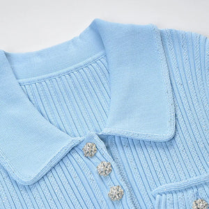 Close-up of a light blue sweater with a collar and decorative buttons on a white background