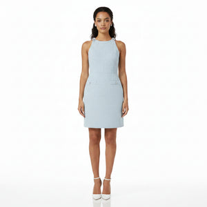 A woman modeling a light blue sleeveless textured dress with side cutouts and white high heels against a plain white background.