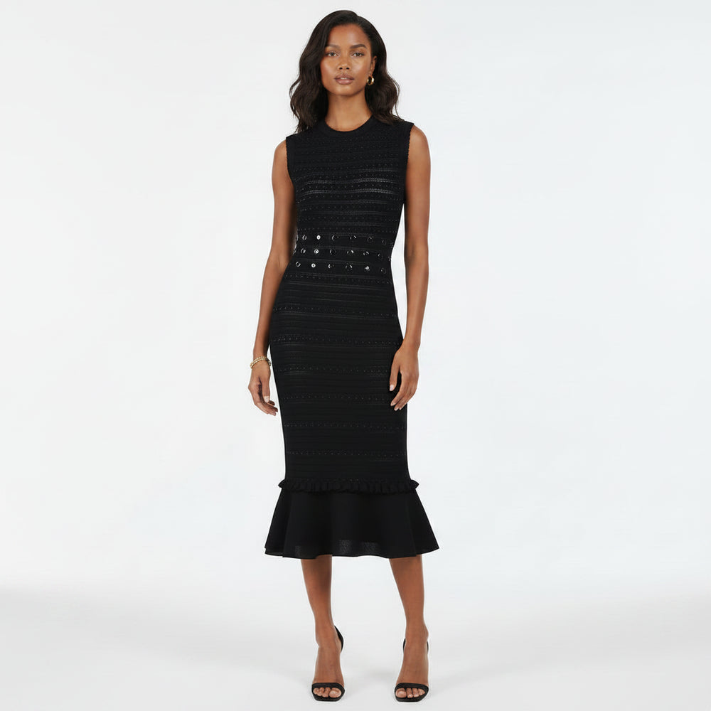 A woman modeling a sleeveless black midi dress with textured horizontal knit lines, a studded waistband, and a ruffled hem, set against a plain white studio background.