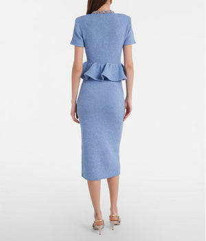 A woman viewed from the back wearing a light blue short-sleeve knit dress with a peplum waist and a beaded neckline, paired with metallic high-heeled sandals against a light gray studio background.