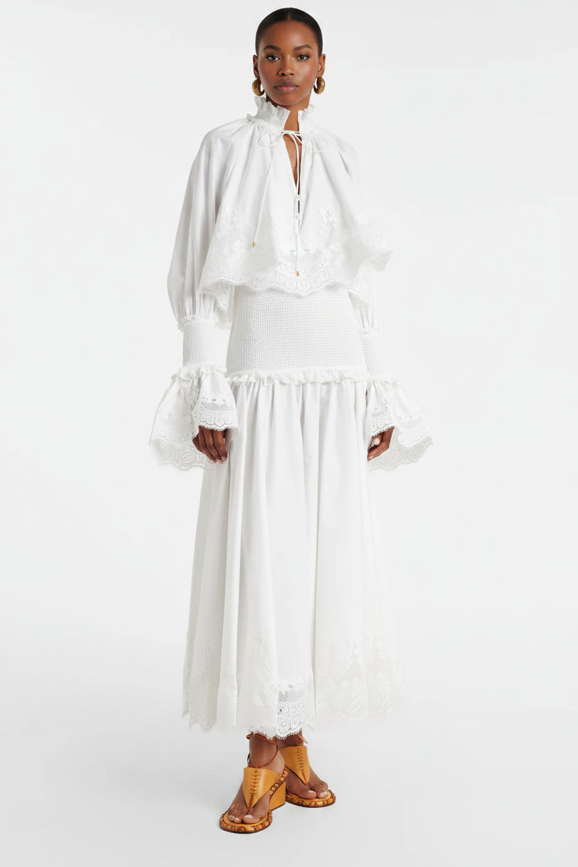 Person wearing a white dress with long sleeves and a skirt, standing against a white background.