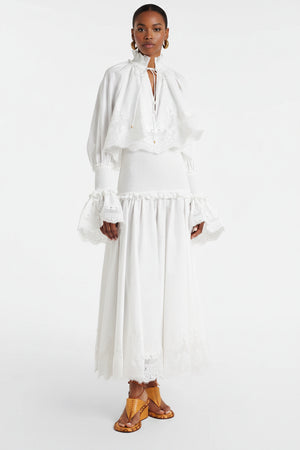 Person wearing a white dress with long sleeves and a skirt, standing against a white background.