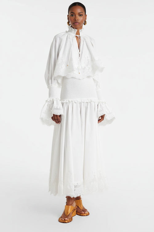Person wearing a white dress with long sleeves and a skirt, standing against a white background.