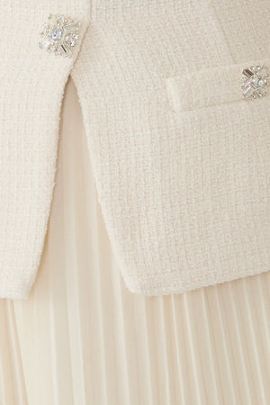 Close-up of a cream-colored tweed jacket with crystal-embellished buttons and a pleated cream skirt.