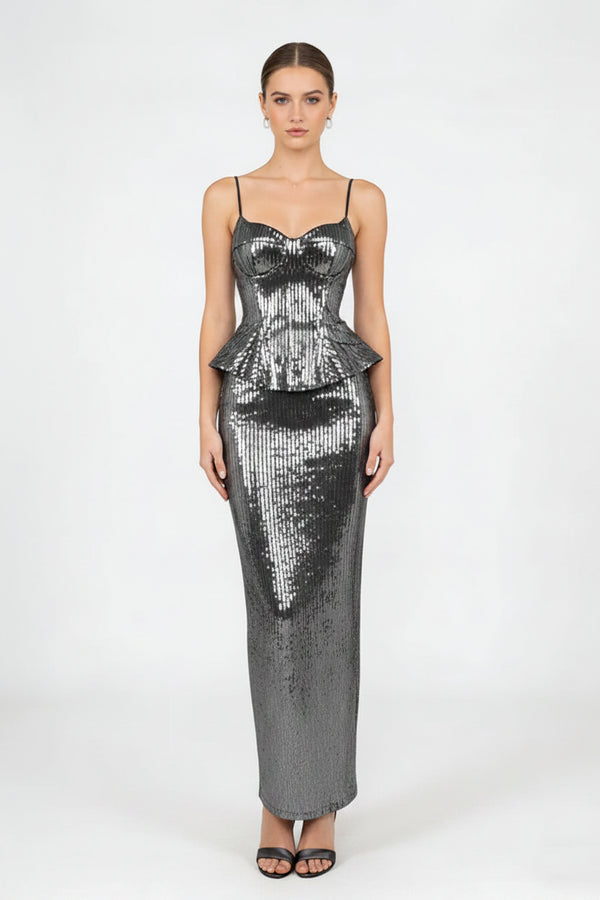A woman modeling a floor-length, bodycon sequined dress in metallic silver with thin spaghetti straps and a sweetheart neckline, paired with a matching sequined clutch bag and black sandals, against a plain light gray studio background.