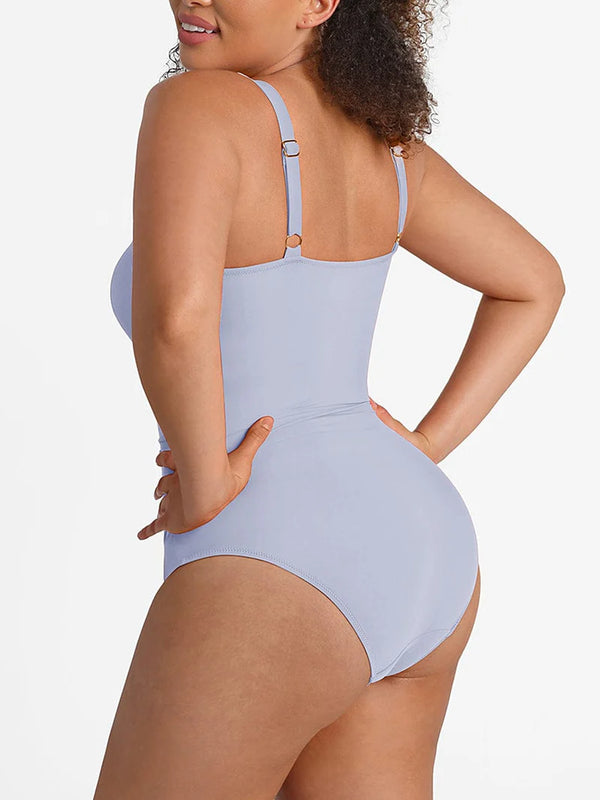 A woman modeling a light periwinkle blue one-piece swimsuit from the back, showing the adjustable shoulder straps and high-cut leg design, against a plain white background.