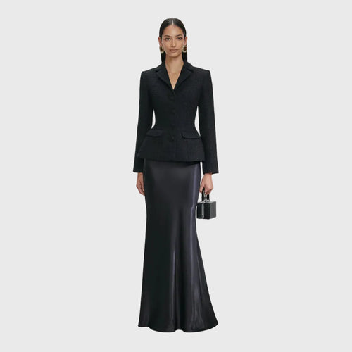 Woman wearing a black suit with a long black skirt on a white background
