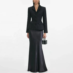 Woman wearing a black suit with a long black skirt on a white background