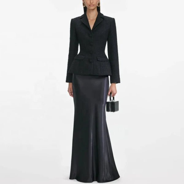 Woman wearing a black suit with a long black skirt on a white background